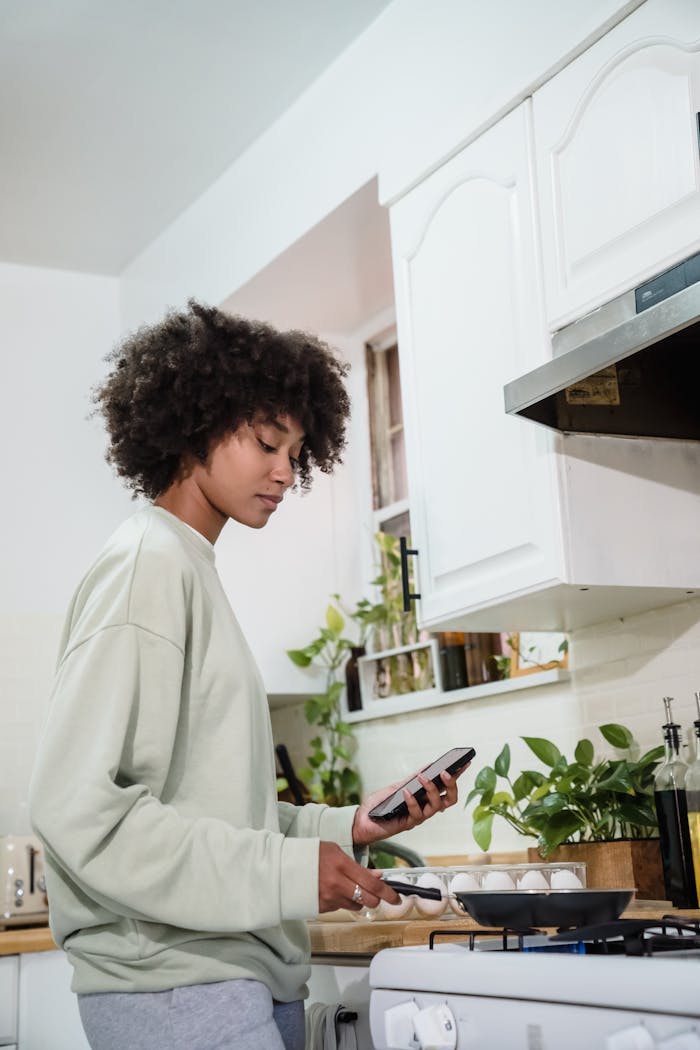 services-01 African American woman cooking in a kitchen while checking her smartphone